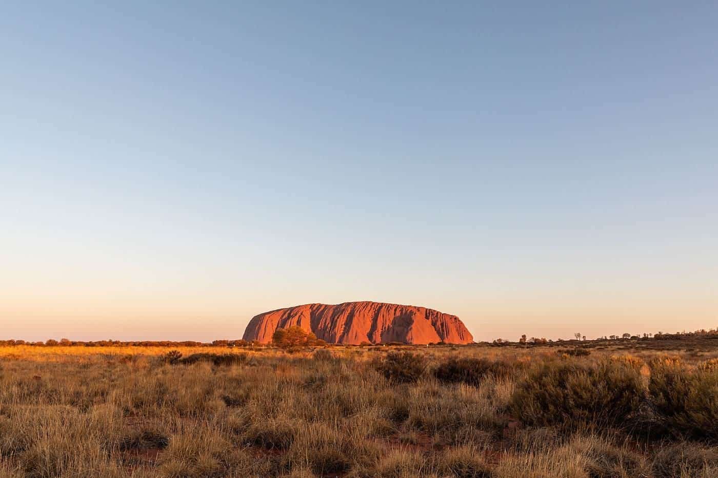 A sunlit red desert landscape near Uluṟu with a clear blue sky